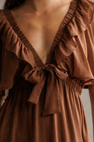 Brown dress with ruffled details and a tie waist on a neutral background
