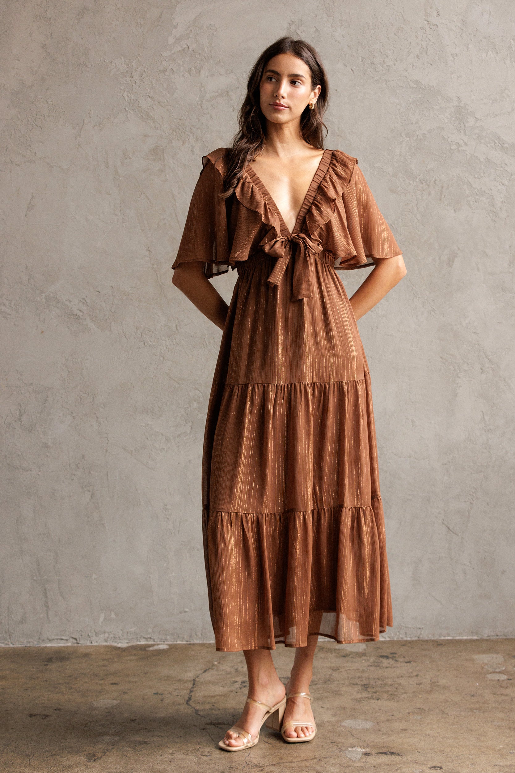 Woman wearing a brown dress against a gray concrete wall