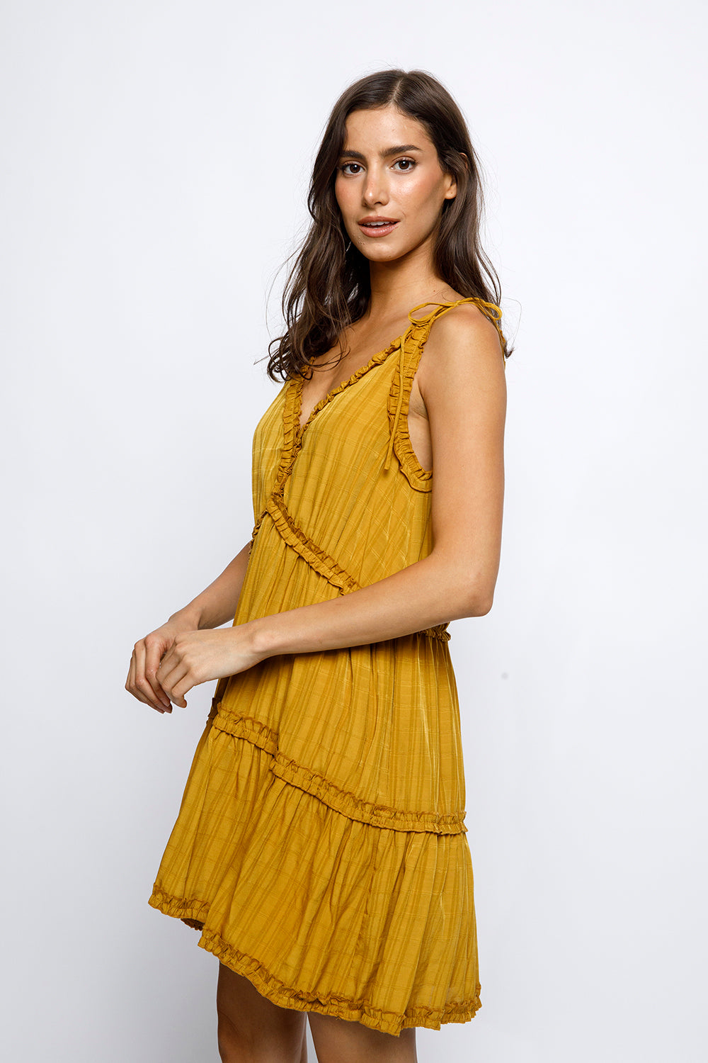 Side view of a woman wearing a mustard yellow dress against a white background