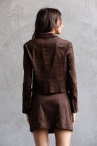 Back view of a woman wearing a brown jacket and skirt set against a gray background