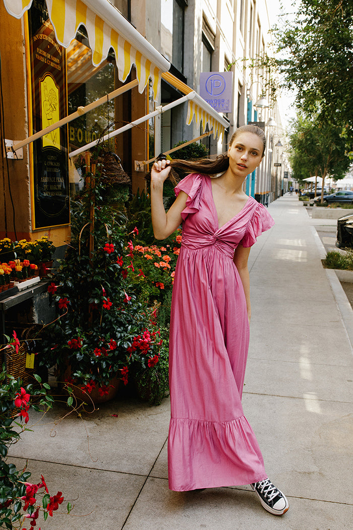 Woman in a pink maxi dress and black sneakers standing in front of a flower store