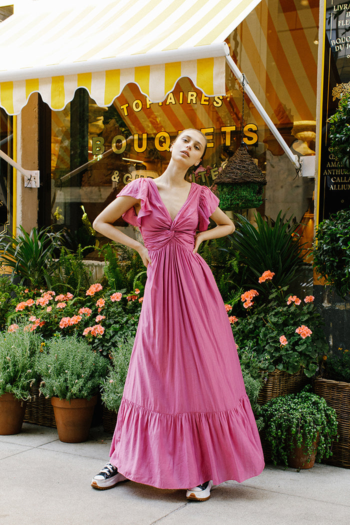 Woman in a pink maxi dress standing in front of a store with a striped awning.