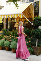 Back view of a woman in a pink maxi dress with an open back standing in front of a store