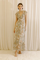 Woman wearing a beige floral dress standing against a plain background