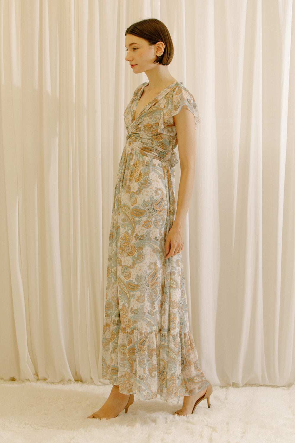 Side view of a woman wearing a beige floral dress standing against a plain background