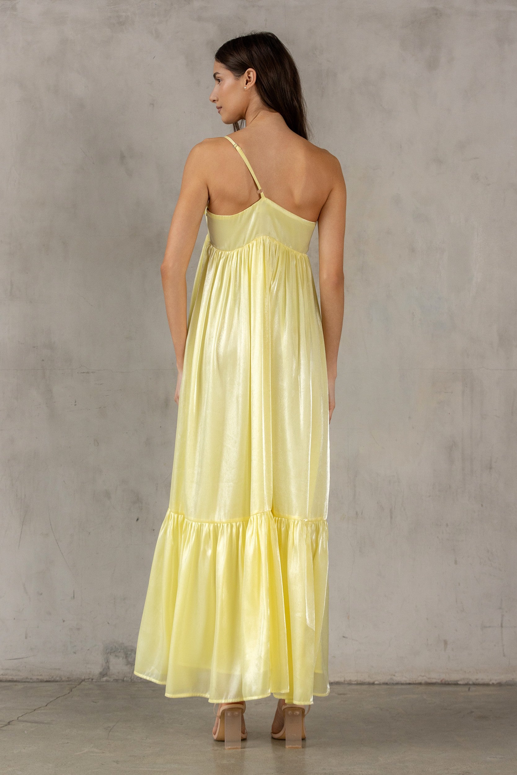 Back of a woman wearing a yellow dress against a gray concrete wall