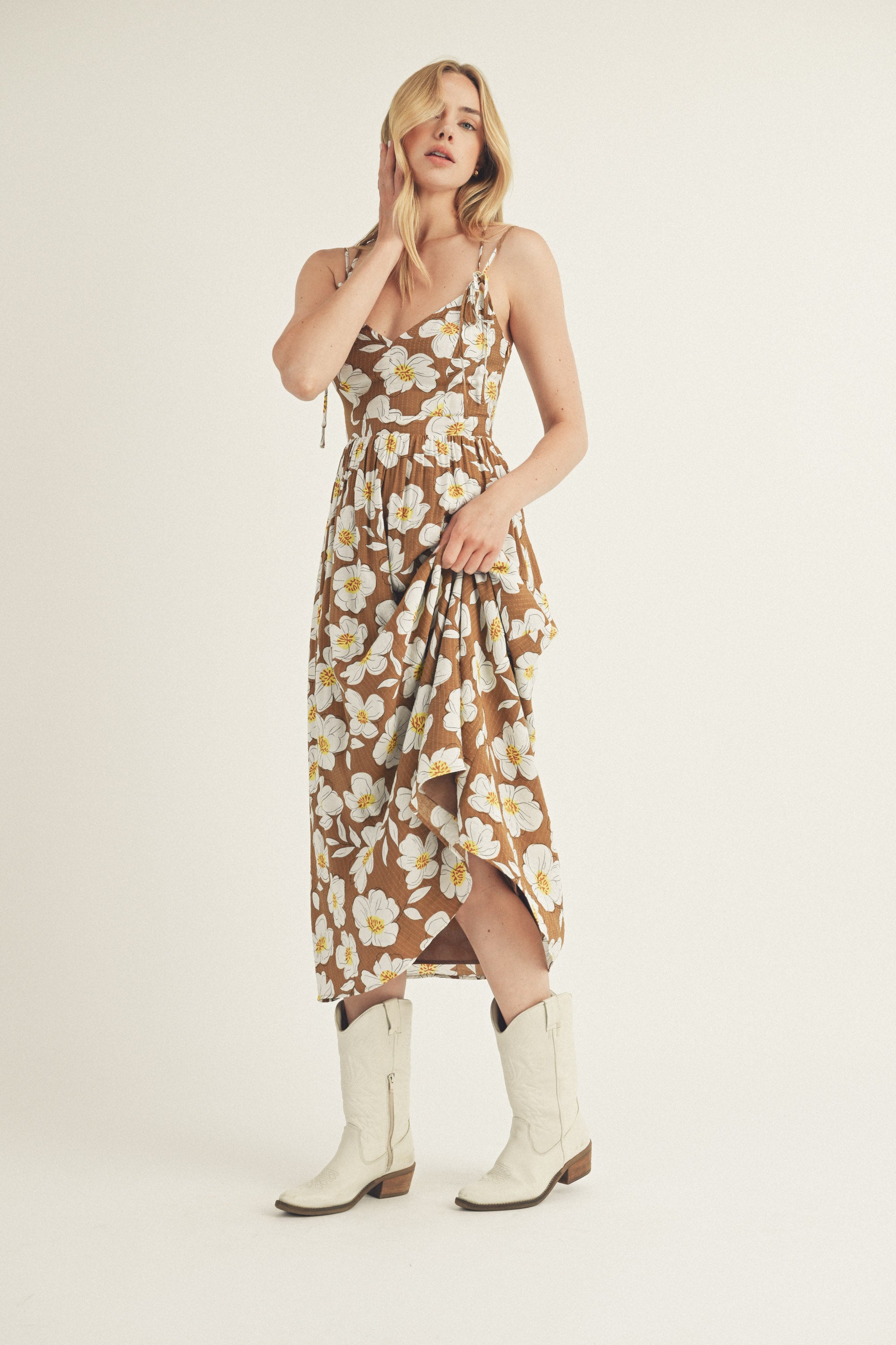Woman wearing a brown and white floral dress and white boots on a plain background