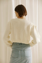 Back view of a woman wearing a cream-colored cardigan against a white curtain background
