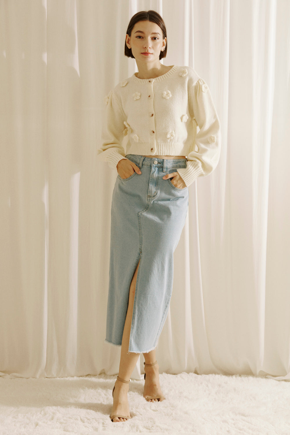 Woman wearing a cream cardigan with floral embellishments against a white curtain background