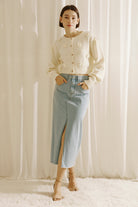Woman wearing a cream cardigan with floral embellishments against a white curtain background