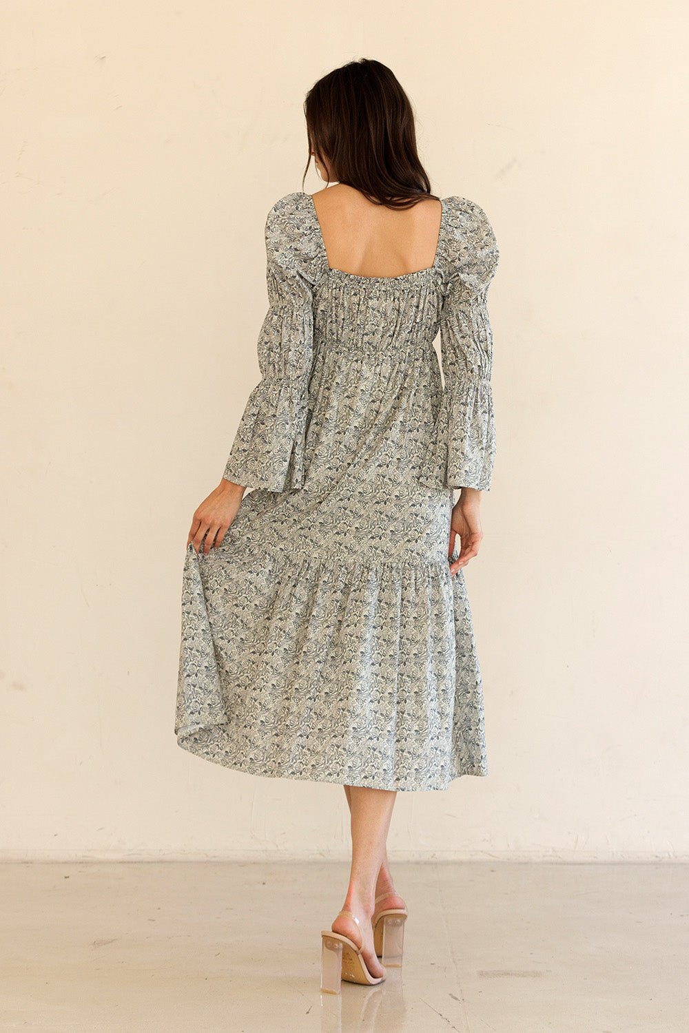 Back view of a woman wearing a navy floral dress with long sleeves against a beige background