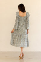 Back view of a woman wearing a navy floral dress with long sleeves against a beige background