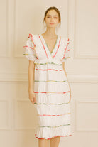 Woman wearing a white dress with colorful stripes against a beige wall.