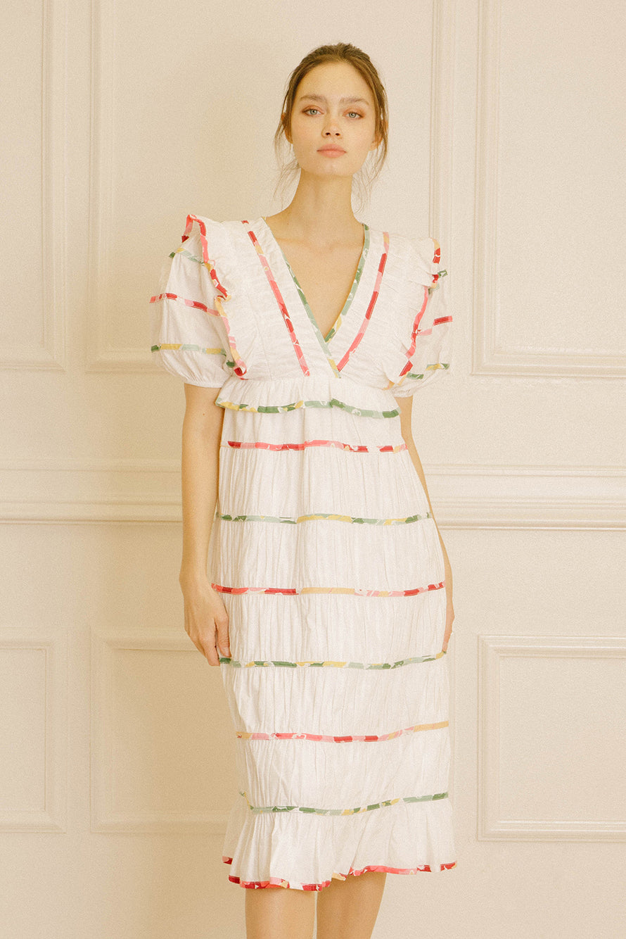 Woman wearing a white dress with colorful stripes against a beige wall.