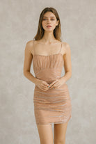 Woman wearing a champagne metallic star print tulle mini dress with ruched fit against a plain background