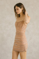 Side view of a woman wearing a champagne metallic star print tulle mini dress with ruched fit against a plain background
