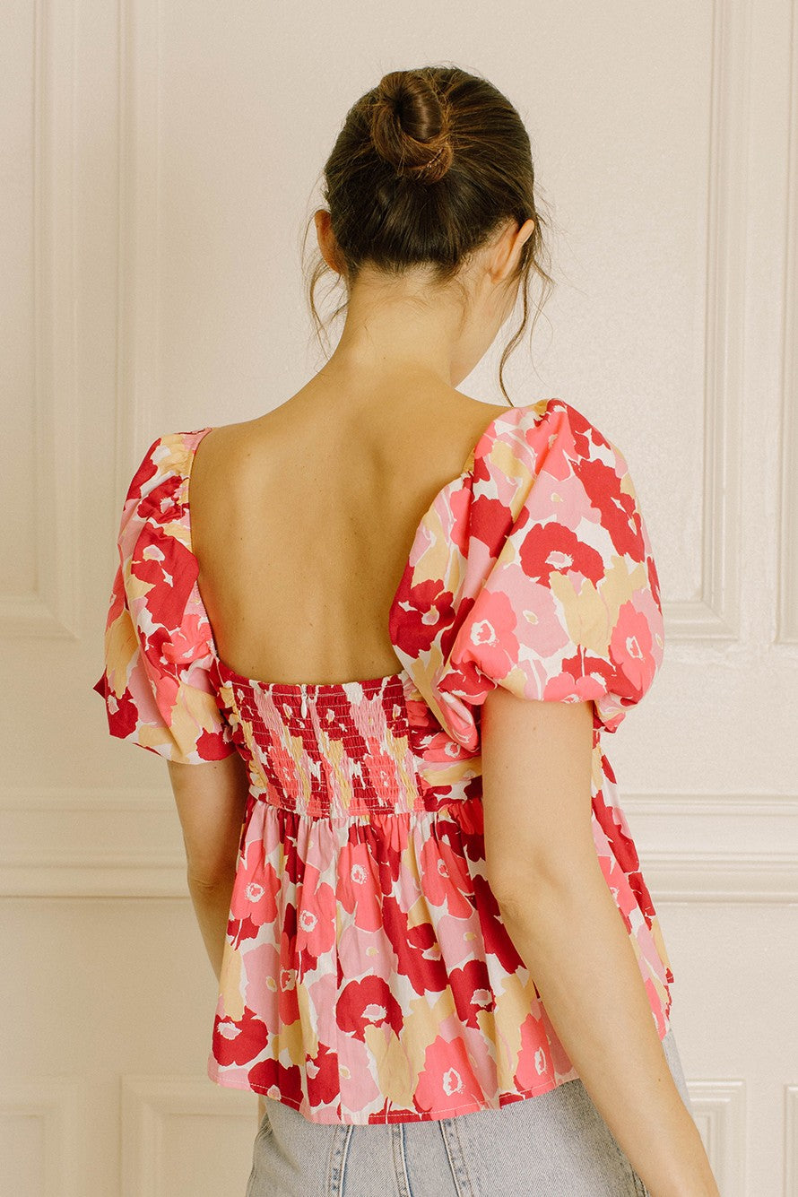 Woman wearing a pink floral blouse with a smocked back in  a beige wall background