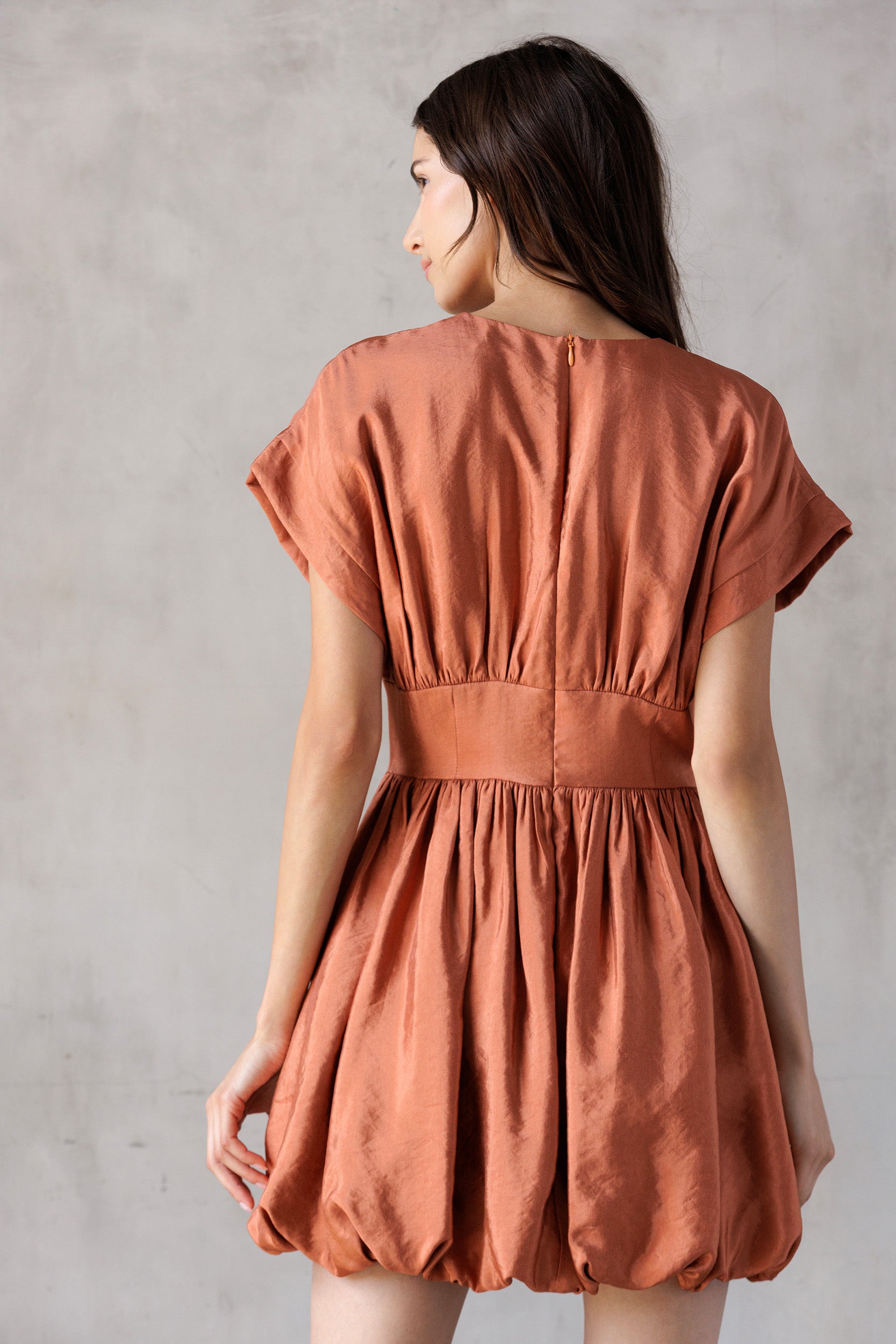 Woman wearing a rust-colored dress against a plain background