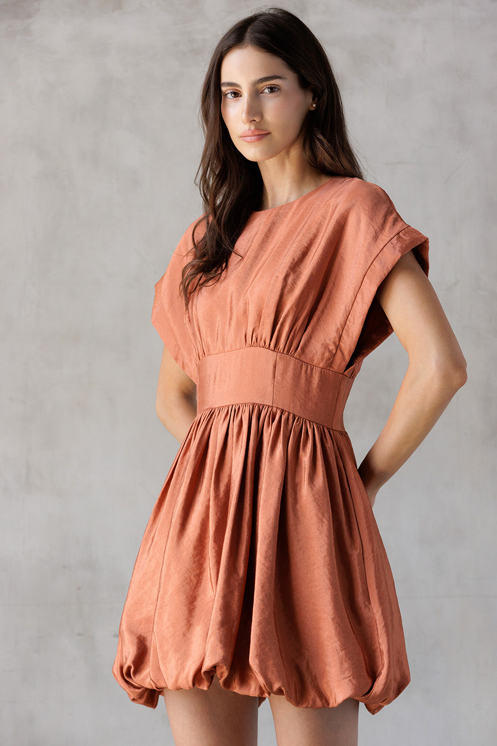 Woman wearing a rust-colored dress against a plain background