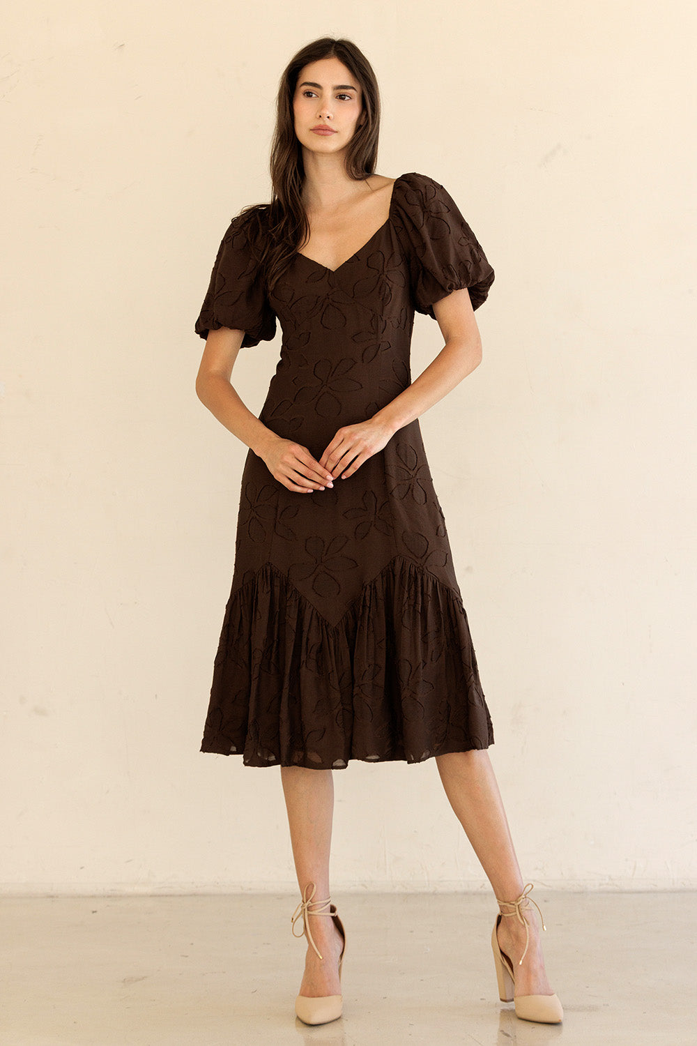 Woman wearing a brown dress with puff sleeves against a beige background