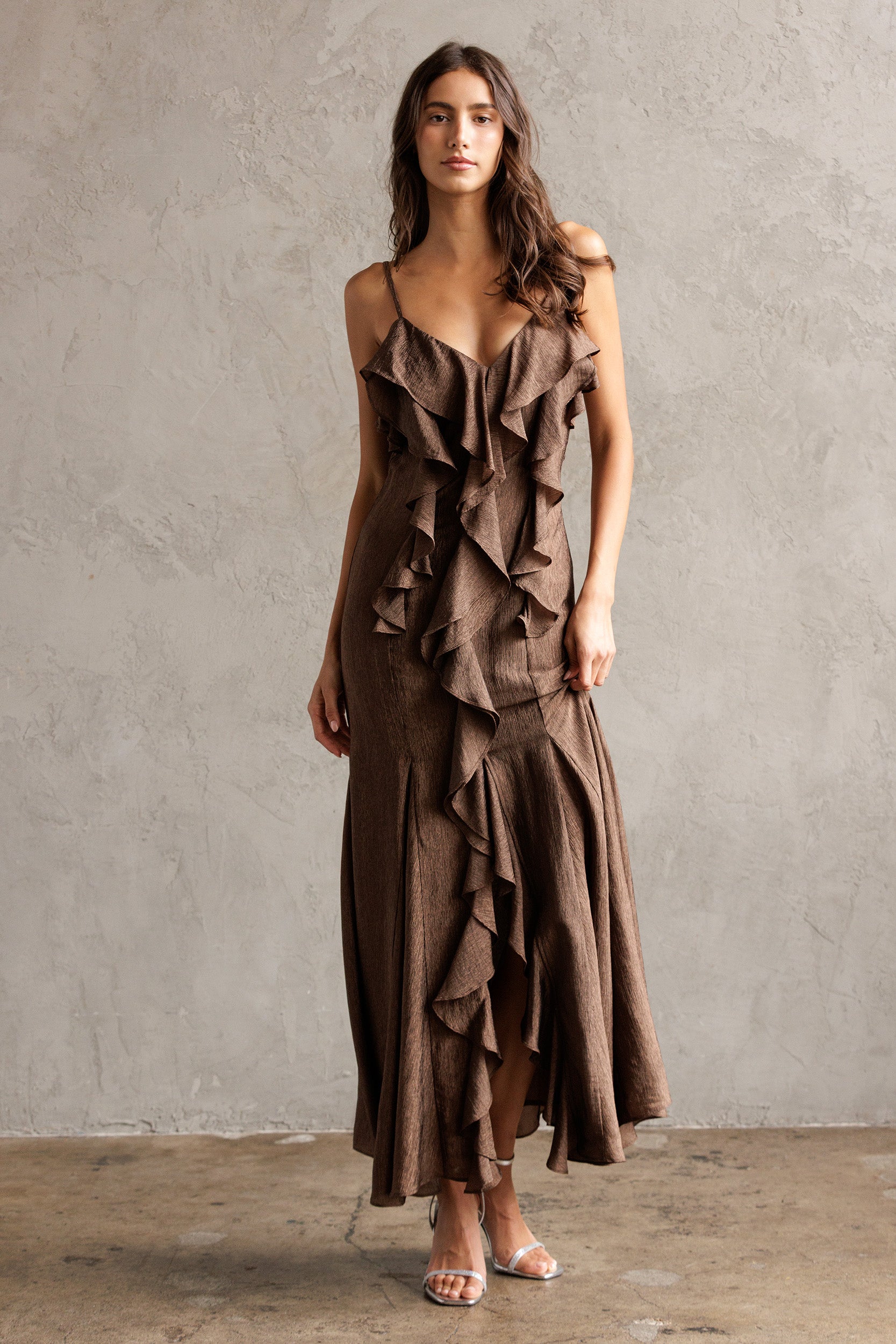 Woman wearing a brown ruffled dress against a plain background