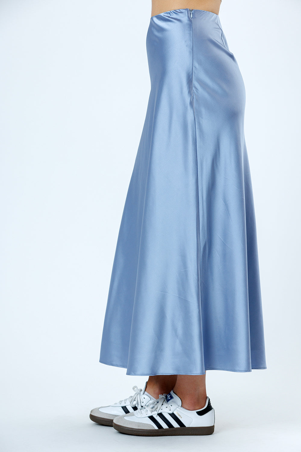 Side view of a light blue satin skirt worn with white Adidas sneakers on a white background