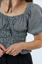Person wearing a black and white checkered blouse with puff sleeves on a plain background
