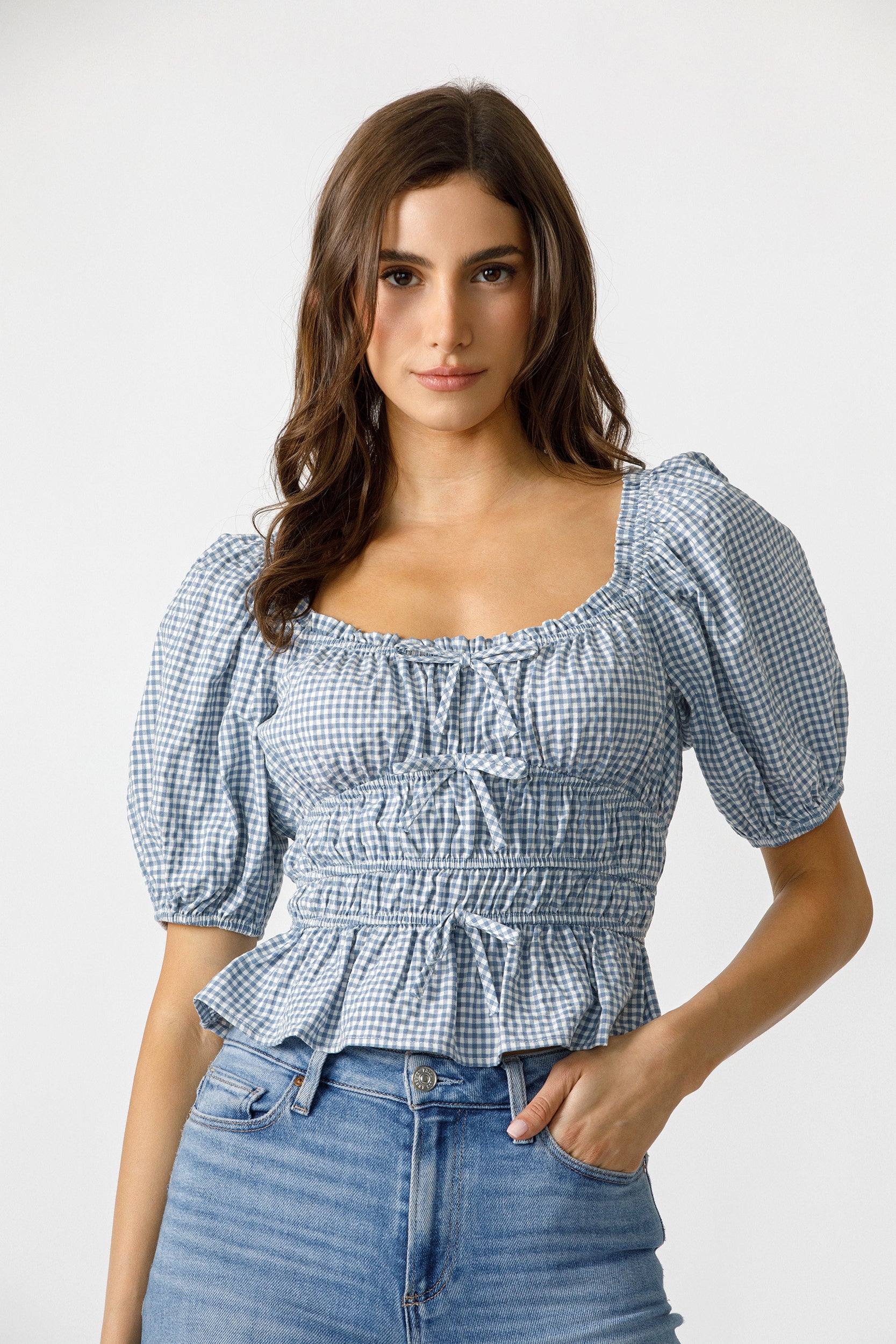 Woman wearing a blue checkered top with puffed sleeves against a white background