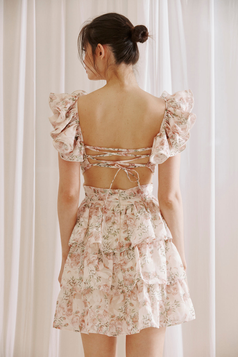 Back view of blush floral ruffle mini dress with open back and lace-up tie