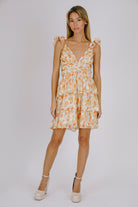 Woman wearing an orange and cream floral dress with beige heels against a plain background