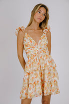 Woman wearing an orange and cream floral dress against a plain background