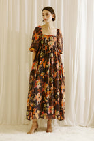 Woman wearing a brown floral dress standing against a white curtain backdrop