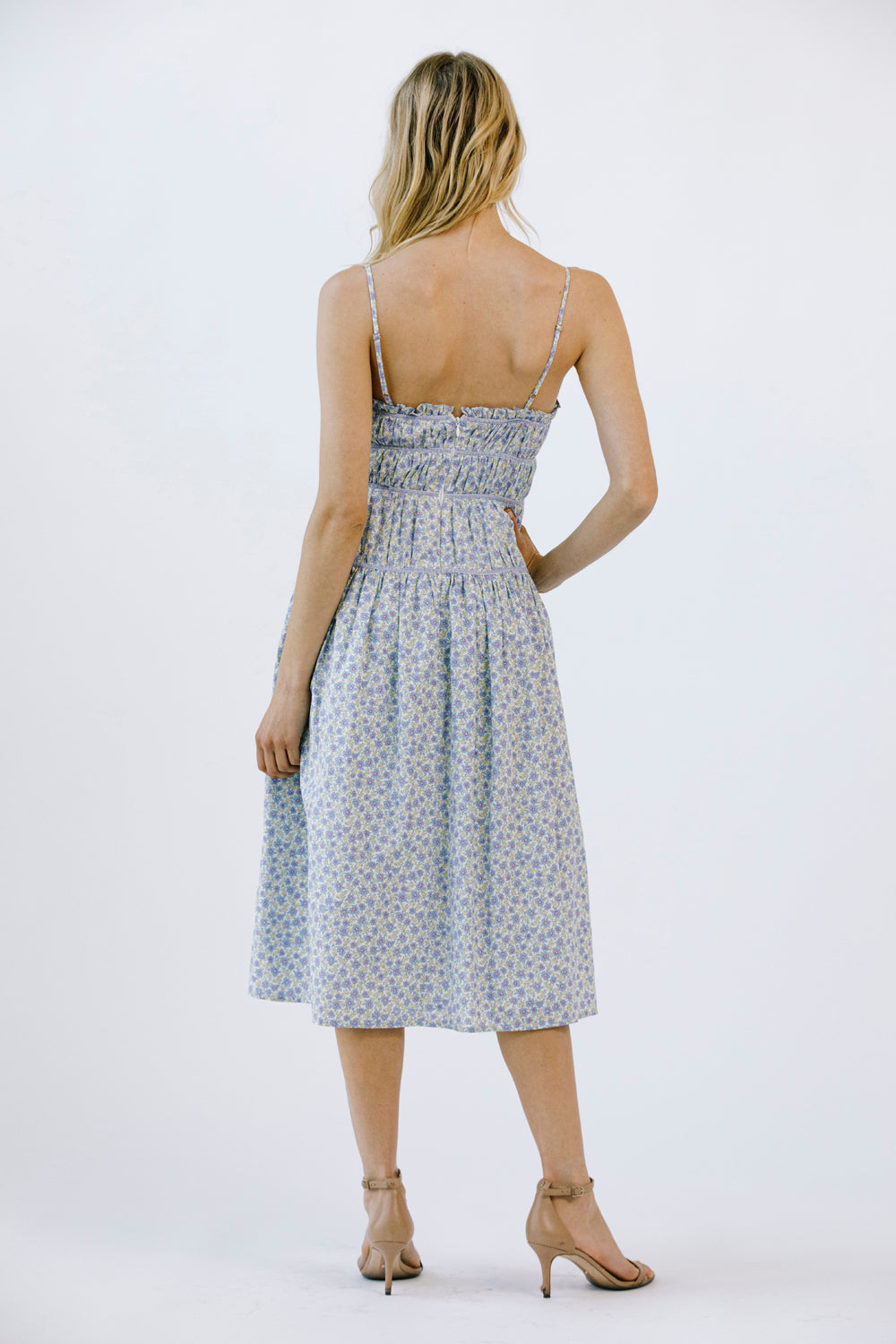 Back view of a woman wearing a blue floral midi dress on a white background