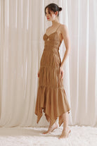 Side view of a woman wearing a brown dress with asymmetrical hem standing against a white curtain background