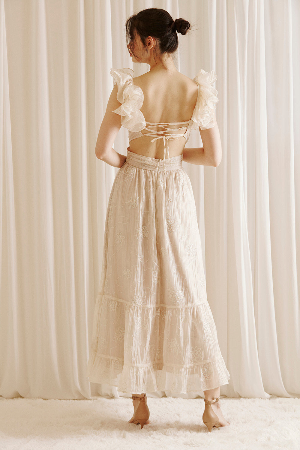 Back view of a woman wearing a beige maxi dress with embroidered flowers
