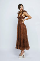 Side view of a model wearing a brown dress with ruffled details on a white background