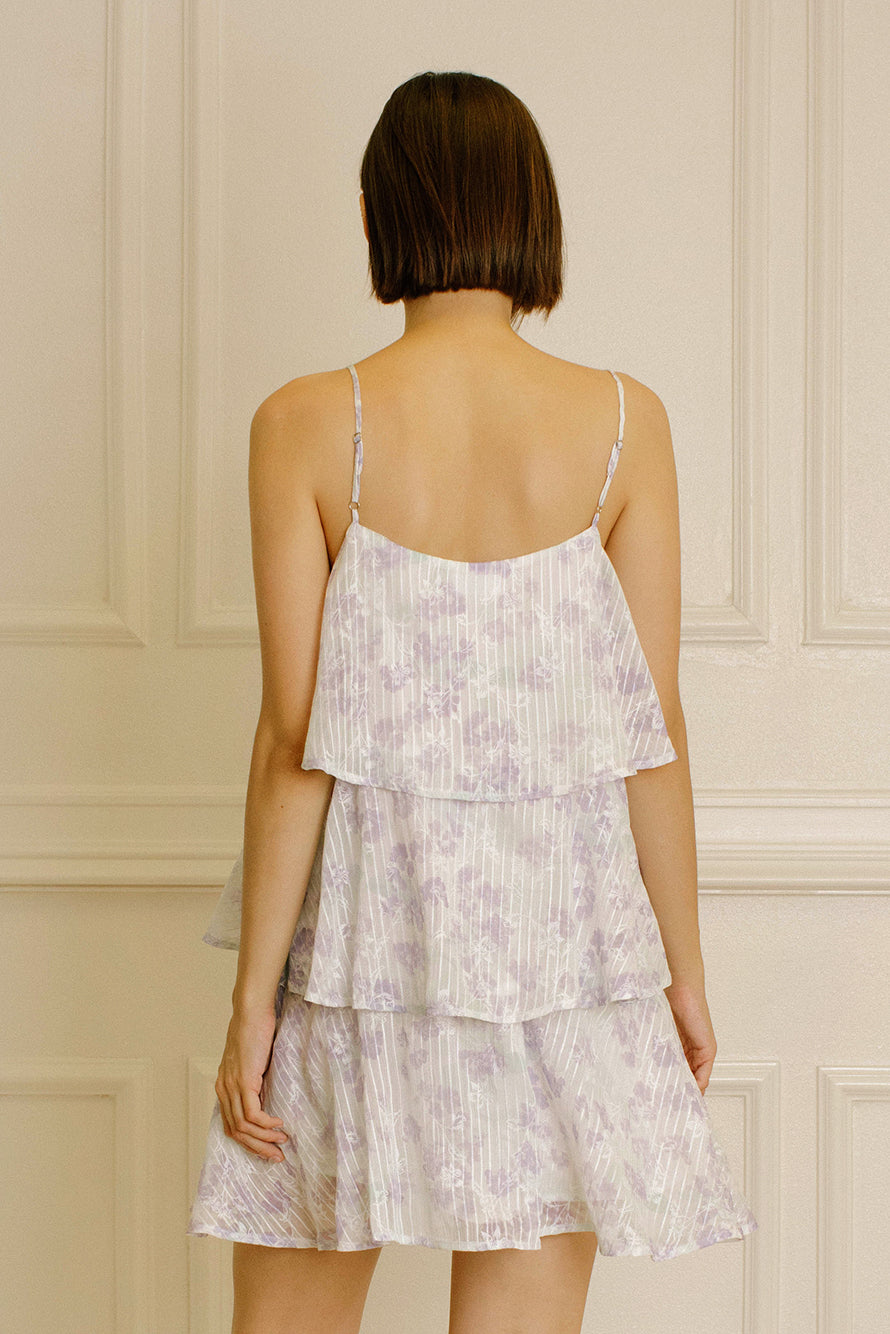 Back view of a woman wearing a lavender slip dress with floral and stripe pattern against a beige wall