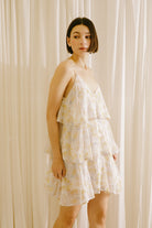 Side view of a woman wearing a yellow slip dress with floral and stripe pattern against a beige curtain background