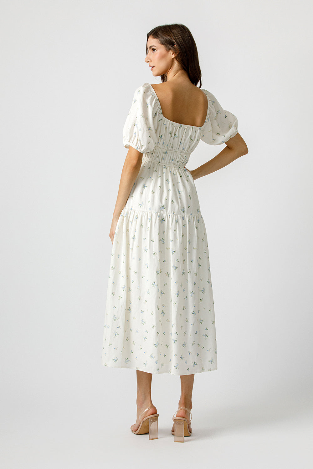 Back view of a woman wearing a cream dress with a floral pattern on a white background