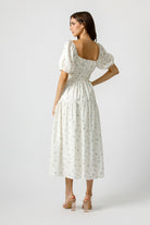Back view of a woman wearing a cream dress with a floral pattern on a white background