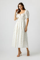 Woman wearing a cream floral dress on a plain background