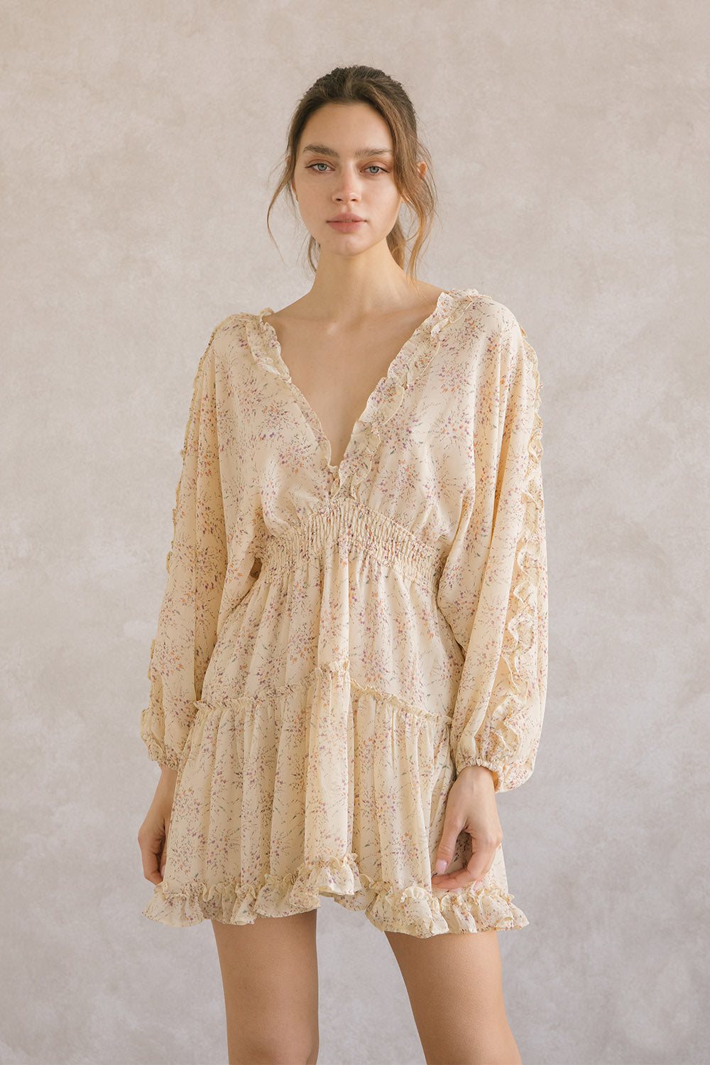 Woman wearing a yellow dress with long sleeves and a v-neckline with ruffle trimming against a plain background