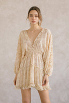 Woman wearing a yellow dress with long sleeves and a v-neckline with ruffle trimming against a plain background