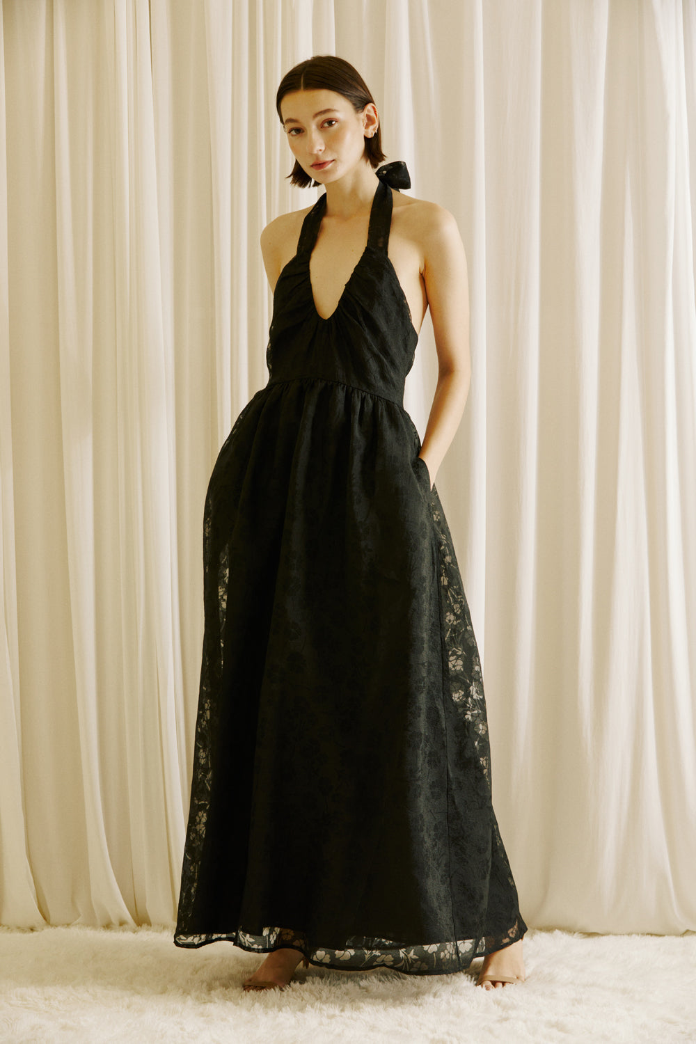 Woman wearing a black halter neck dress against a beige curtain background