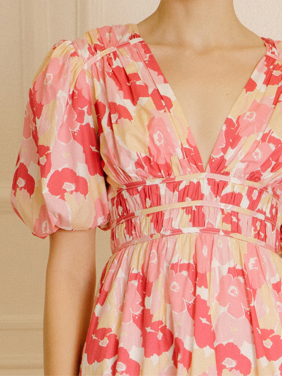 Pink and beige dress with a big floral pattern against a beige wall