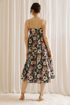 Back view of a woman wearing a navy floral midi dress standing against a white curtain background 