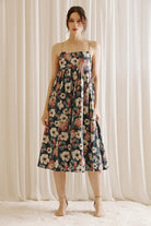 Woman wearing a navy floral midi dress standing against a white curtain background 