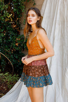 Woman wearing a floral dress standing outdoors with greenery and a white curtain in the background