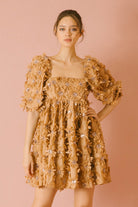Woman wearing a caramel dress with 3D floral detail throughout against a pink background