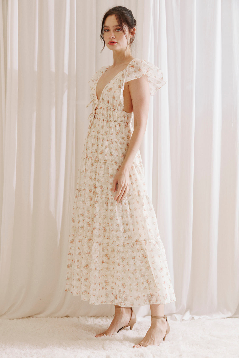 Side view of a woman wearing a floral dress against a white curtain background